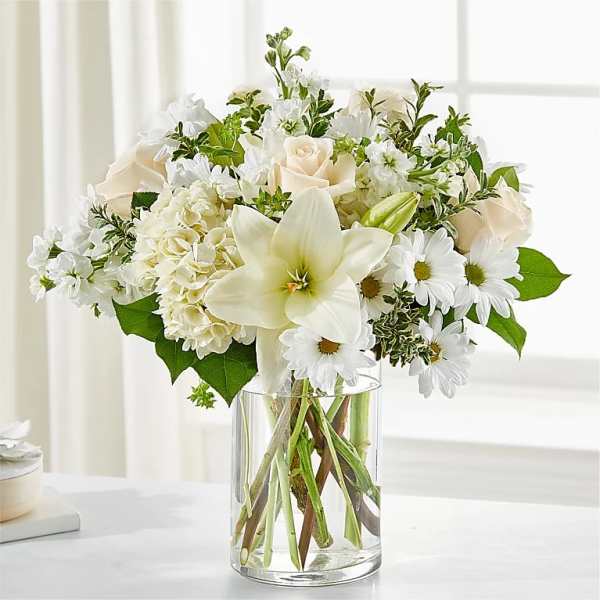 White roses, lilies, and daisies arranged in a clear glass vase