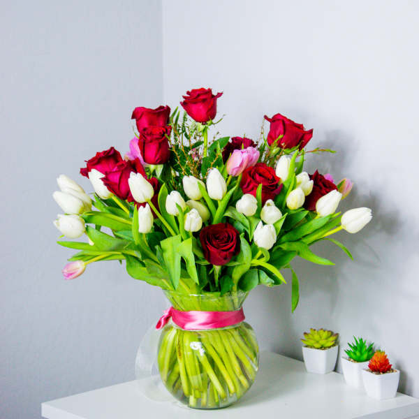 Bouquet of red roses and white tulips in a glass vase with a pink ribbon