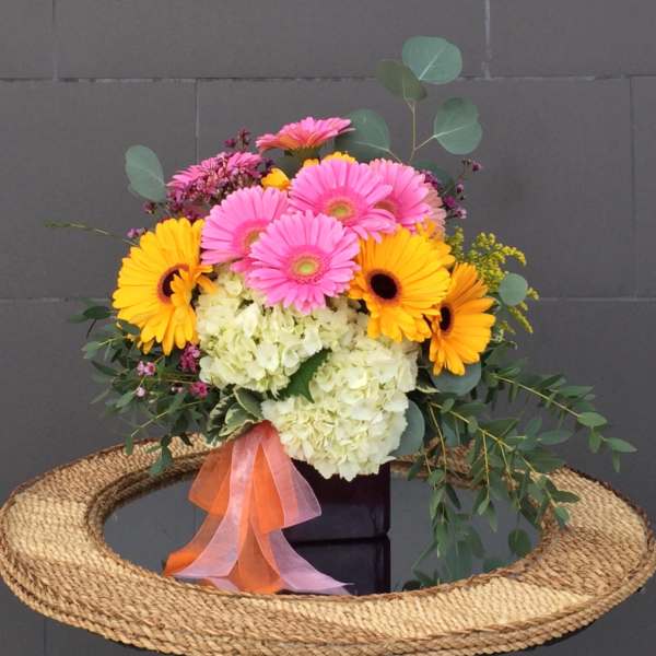 Bouquet of pink and yellow gerbera daisies with white hydrangea in a black box