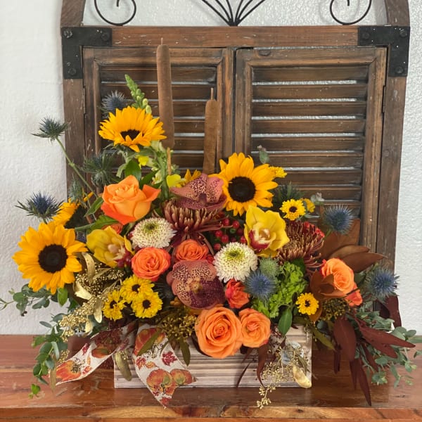 Mixed bouquet with sunflowers, orange roses, and orchids in a wooden container
