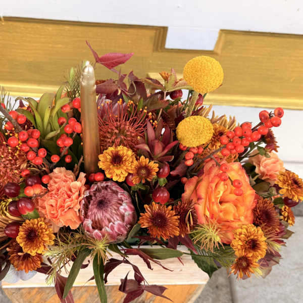 Autumn floral centerpiece with orange blooms and red berries around a candle