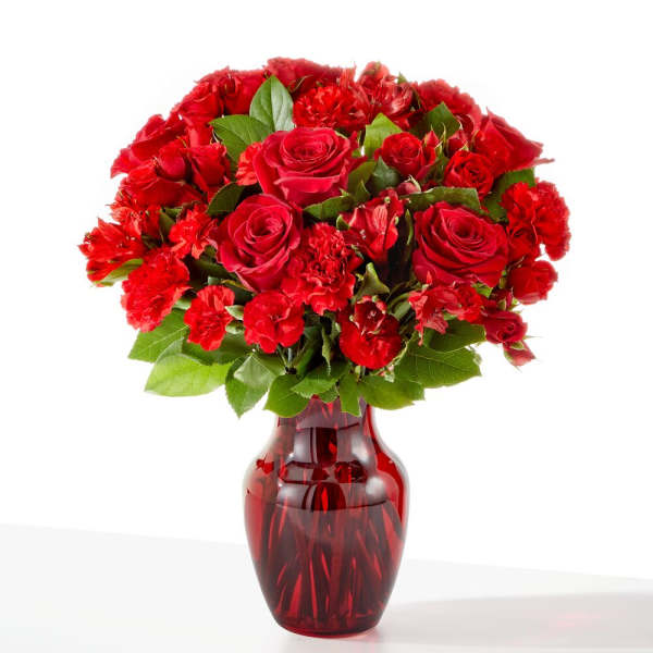 Red roses and carnations arranged in a red glass vase