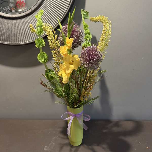 Yellow flowers and purple allium in a green vase with a ribbon