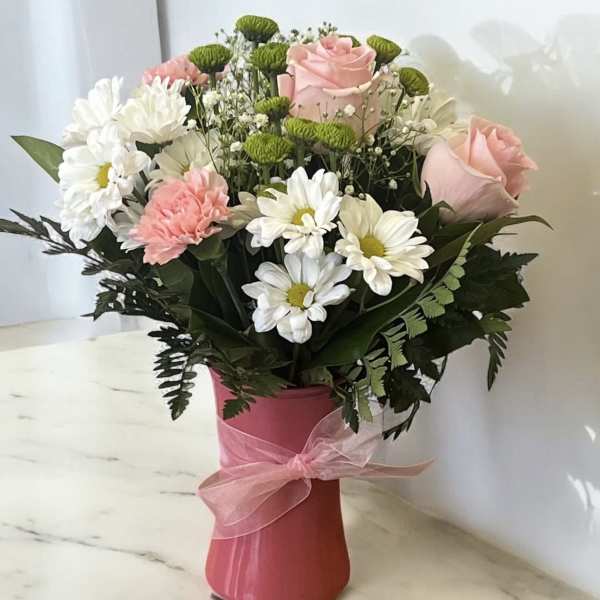 Pink roses and white daisies in a pink vase with a ribbon