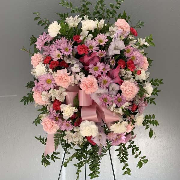 Pink and white floral wreath on a stand with a satin ribbon