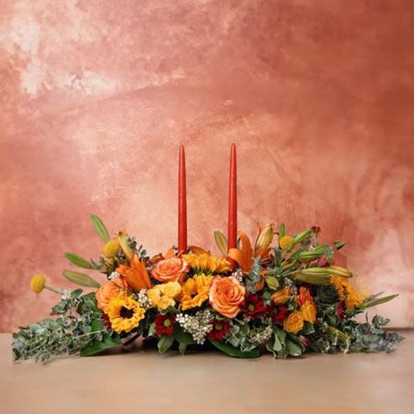 Low floral centerpiece with orange and yellow flowers and two red taper candles