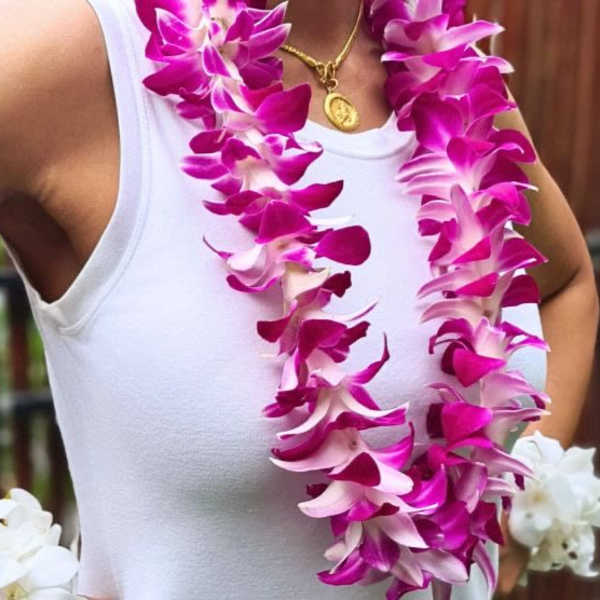 Woman wearing two magenta and white orchid leis over a white top.