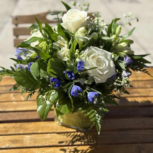 White roses and blue flowers arranged in a glass vase