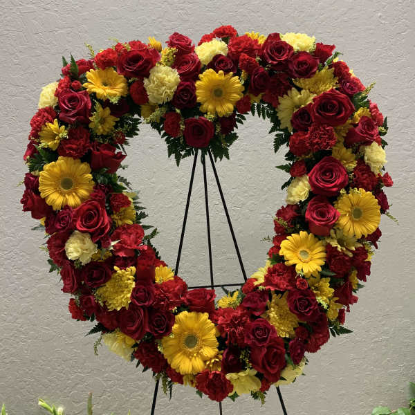 Heart-shaped floral wreath with red roses and yellow daisies on a stand