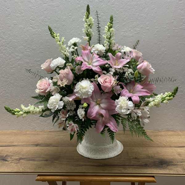 Pink lilies and roses arranged in a white vase with white filler flowers