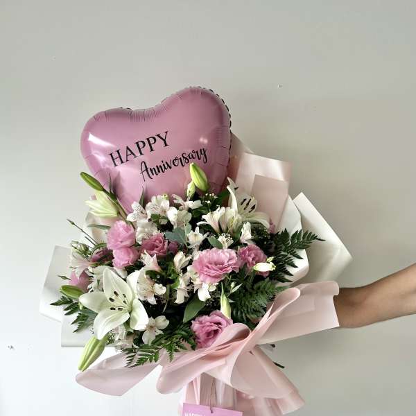 Pink anniversary balloon above a bouquet of white lilies and pink flowers