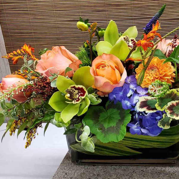 Mixed floral arrangement in a rectangular glass vase with orange and pink blooms