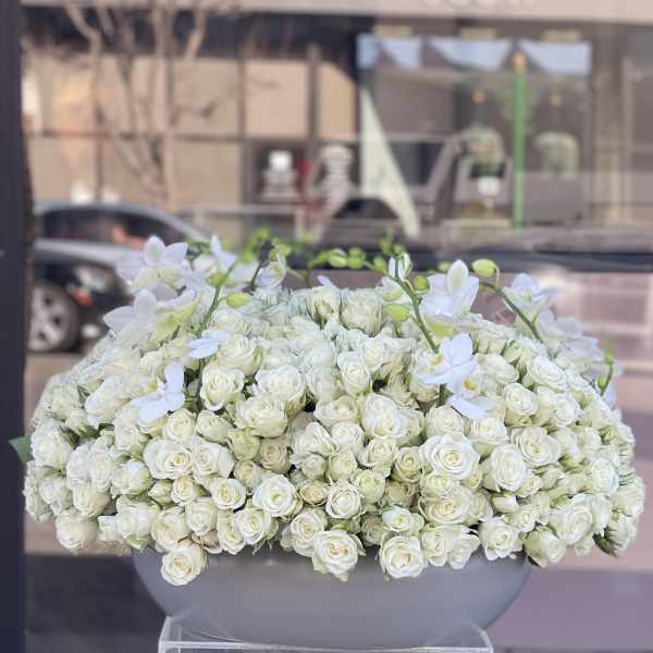Large white rose arrangement in a gray container with white orchid stems
