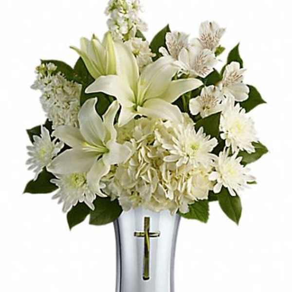 White lilies and daisies arranged in a silver vase with a cross