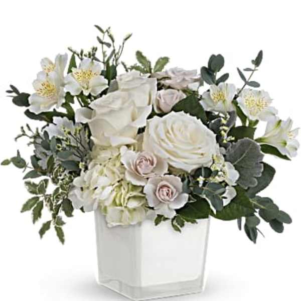 White roses and pale flowers arranged in a clear square vase