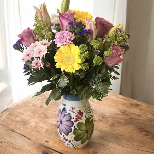 Mixed bouquet in a painted ceramic vase with pink, yellow, and purple flowers.