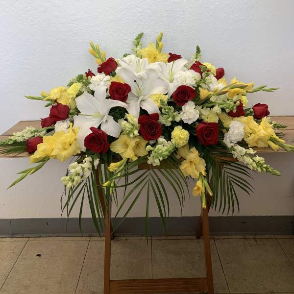 Large floral spray with red roses, white lilies, and yellow flowers on a stand