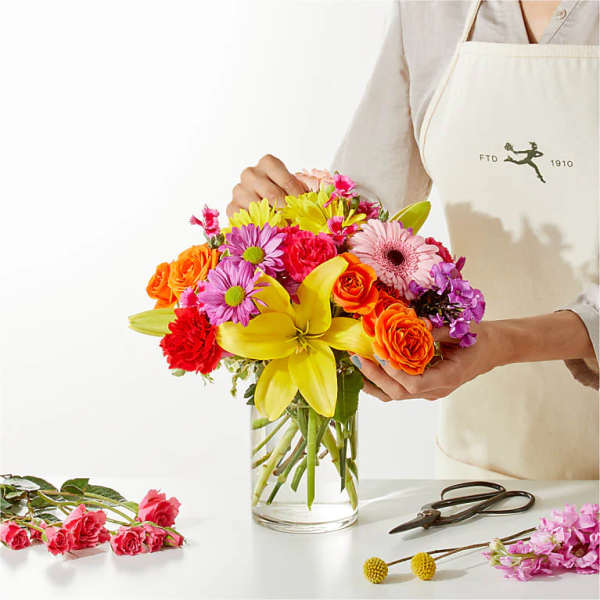 Colorful mixed bouquet in a clear glass vase with a large yellow lily