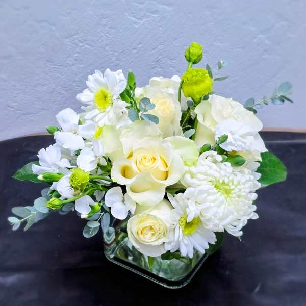 White and pale yellow floral arrangement in a square glass vase