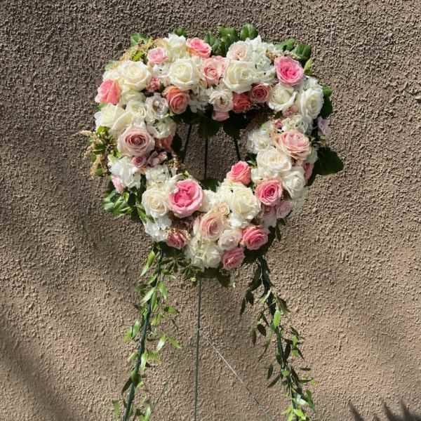Heart-shaped floral wreath of pink and white roses on a stand