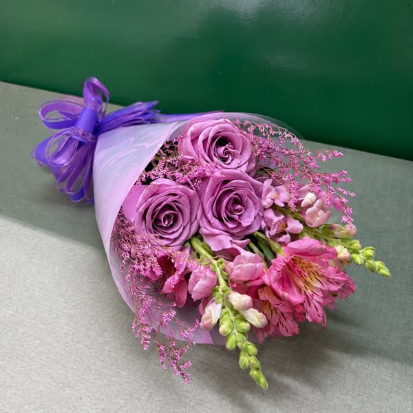 Bouquet of lavender roses and pink flowers wrapped in white paper with a purple ribbon