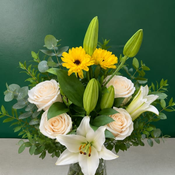 White lilies and cream roses in a glass vase with yellow flowers