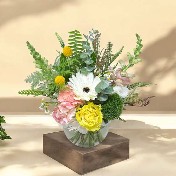 Mixed flower arrangement in a clear glass vase with white, yellow, and pink blooms