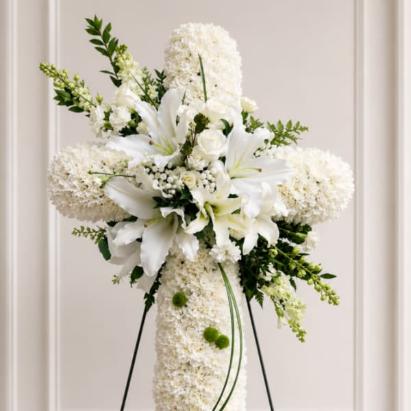White floral standing cross with lilies and roses on an easel