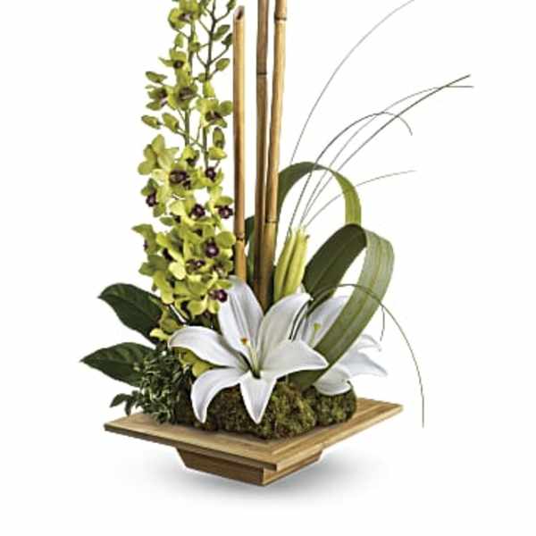White lilies with green orchids and bamboo in a wooden container