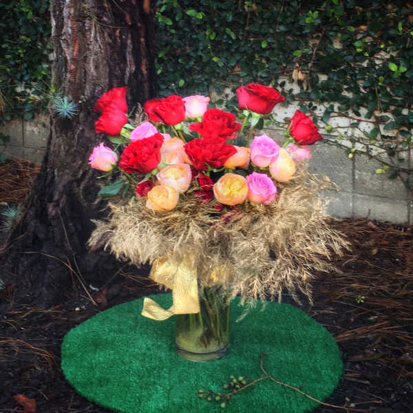 Bouquet of red, pink, and peach roses in a glass vase with a gold ribbon