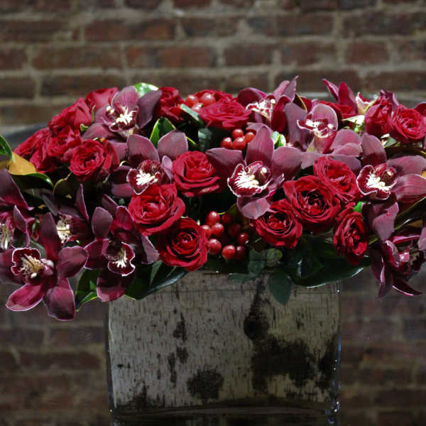 Red roses and burgundy orchids arranged in a square vase