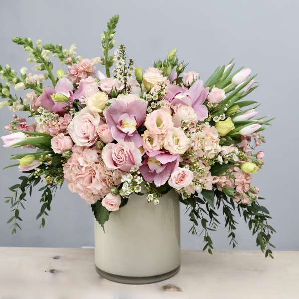 Large pastel pink and white flower arrangement with roses, orchids, and tulips in a white cylinder vase