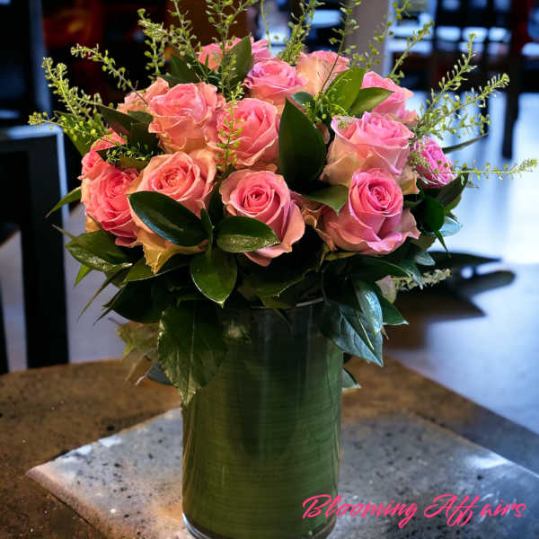 Pink roses arranged in a tall green vase with glossy foliage