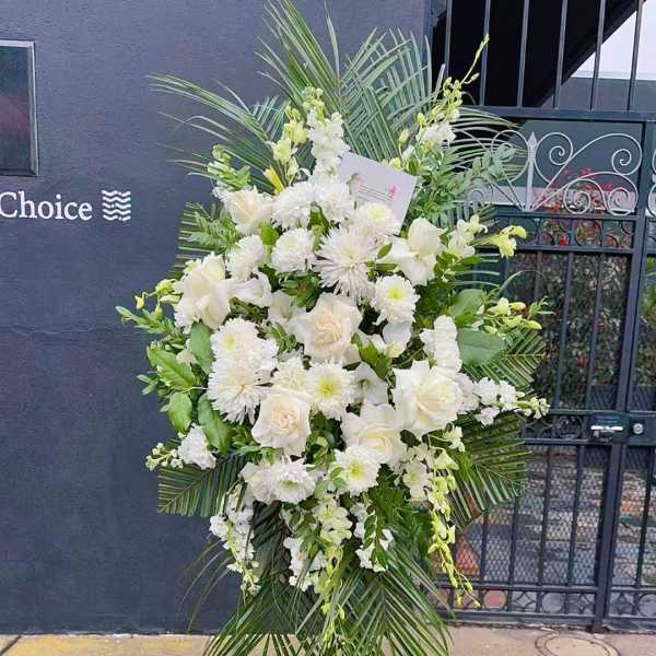 Tall white floral standing spray on an easel with palm fronds