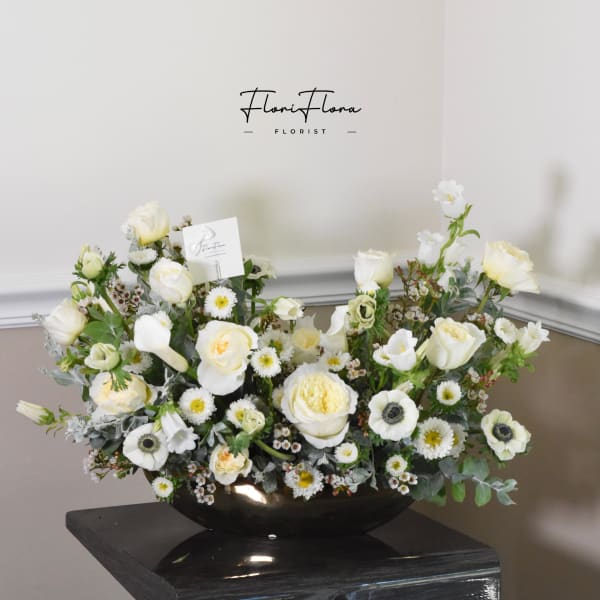 White floral arrangement in a black bowl vase with roses and daisies