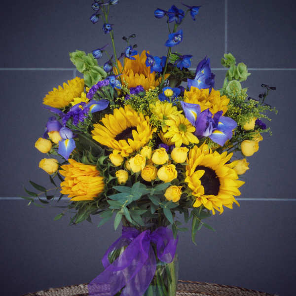 Bouquet of yellow sunflowers and blue flowers in a glass vase with a purple ribbon