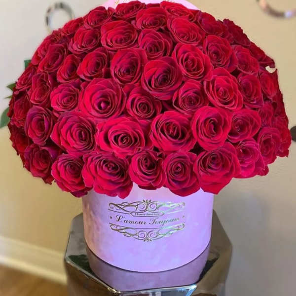 Large dome of red roses arranged in a pink round hat box with gold script on the front