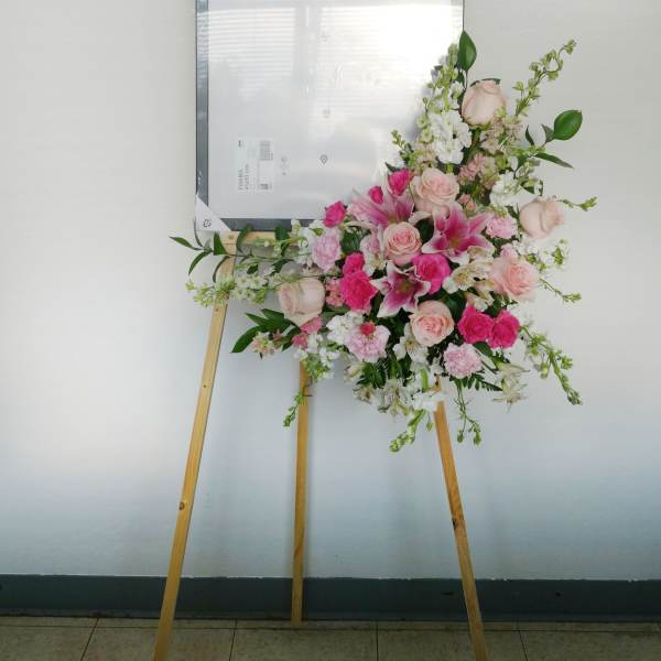 Pink and white floral spray on a wooden easel with a framed sign