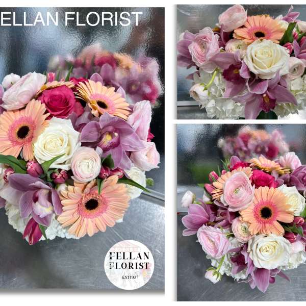 Low round bouquet of pink and peach blooms with white roses in a clear glass vase
