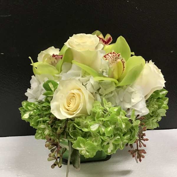 White roses and green orchids in a low glass vase