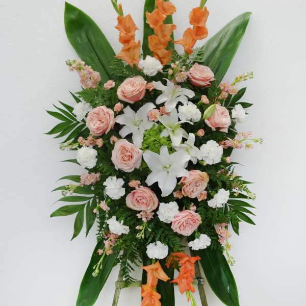 Standing floral spray with peach roses, white lilies, and orange gladiolus