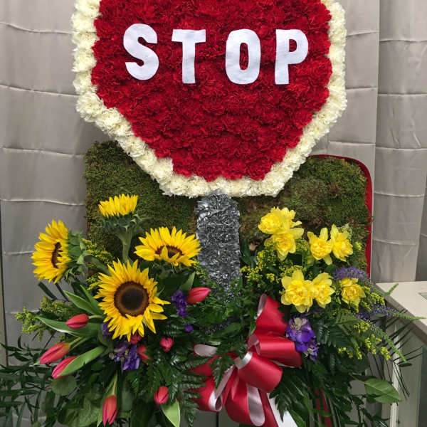 Large floral stop-sign tribute with red and white flowers and sunflowers below