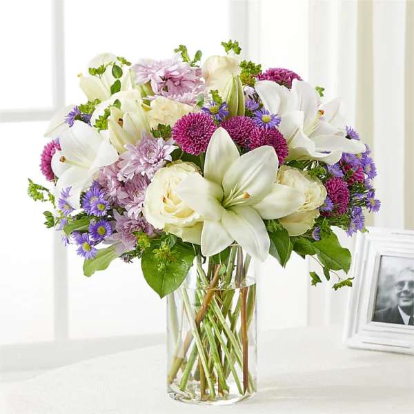 Bouquet of white lilies, cream roses, and purple flowers in a clear glass vase