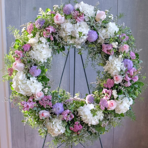 Large floral wreath with pink roses, white hydrangeas, and purple blooms on a stand