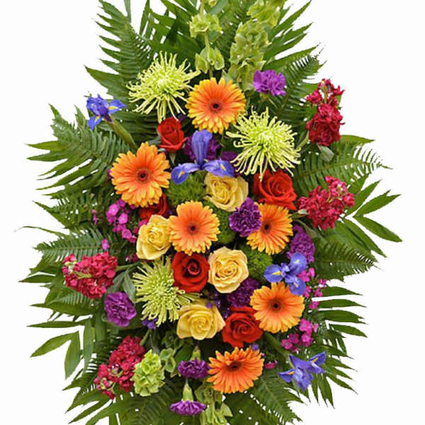 Tall standing spray of bright mixed flowers including orange gerberas, roses, and purple blooms on a green foliage backdrop.
