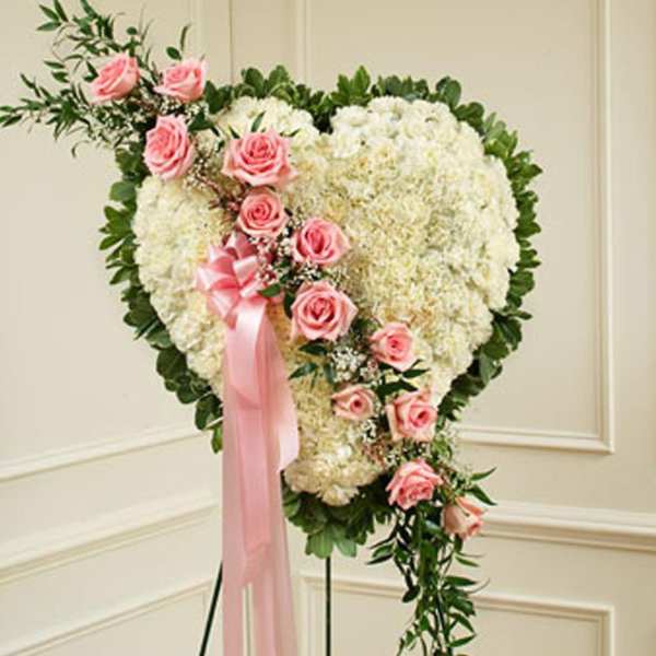 Heart-shaped white floral standing spray with cascading pink roses and ribbon on an easel