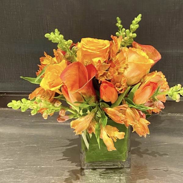 Orange and yellow floral arrangement in a square glass vase