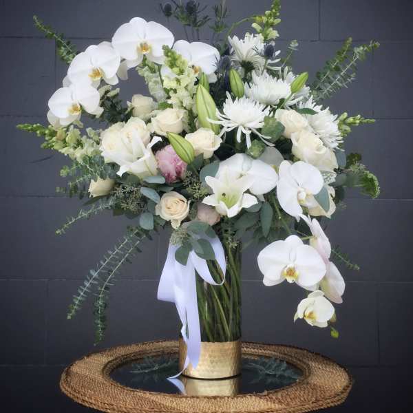 White orchids and roses in a tall glass vase with a ribbon