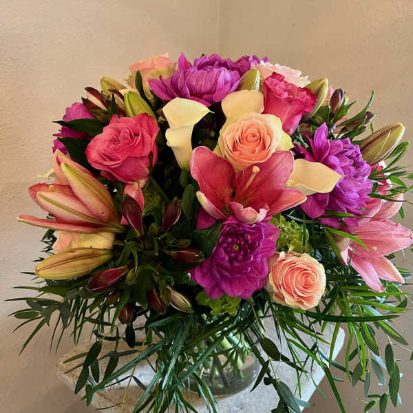Mixed bouquet of pink lilies, roses, calla lilies, and purple blooms in a glass vase