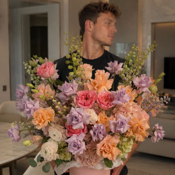 Large pastel bouquet in a pink hat box held by a man indoors
